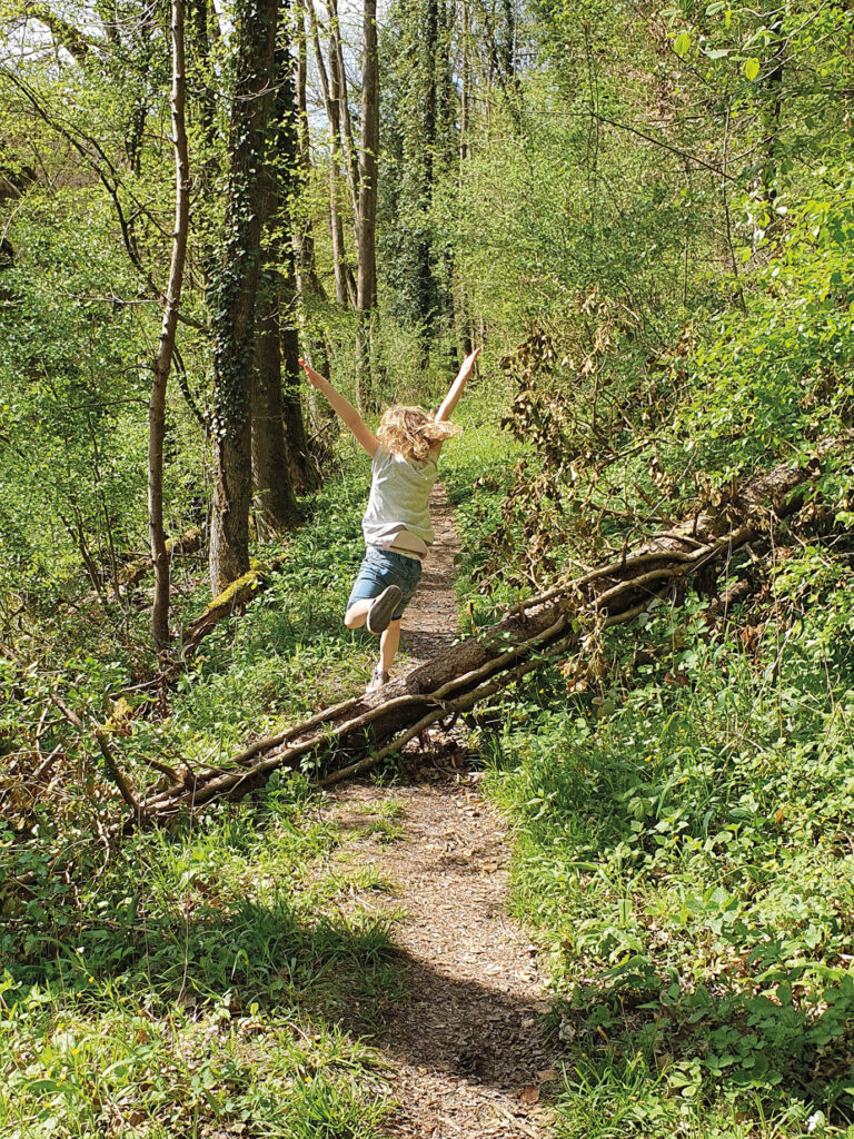 Ein kleines Mädchen das in einem Wald über ein Baumstamm springt